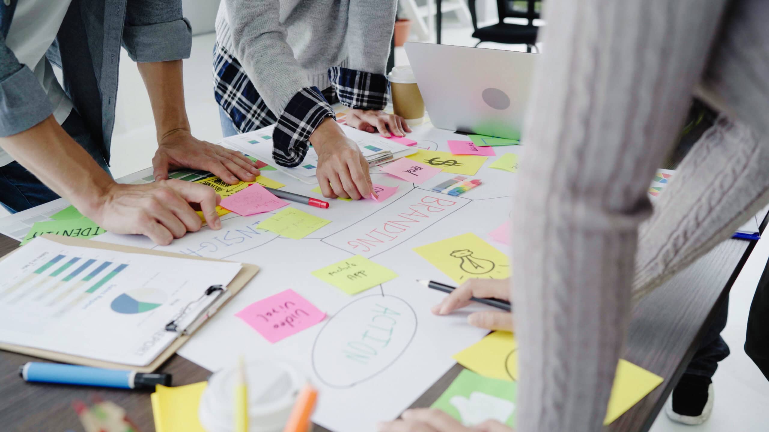 Mãos em cima de uma mesa de trabalho cheia de post its coloridos com anotações.
