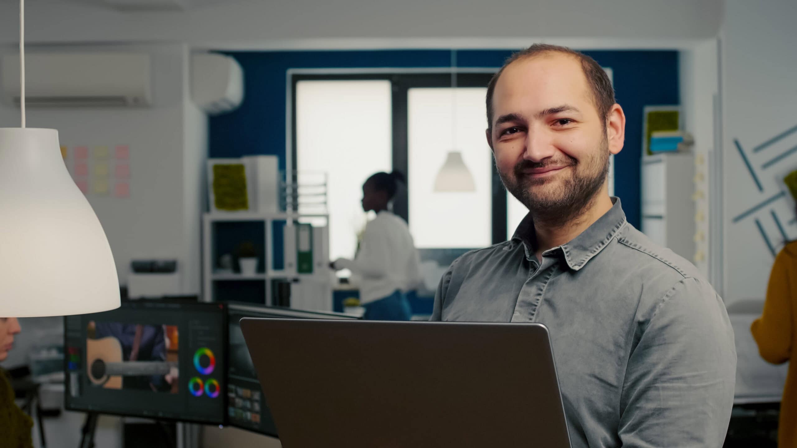 Homem sorrindo para foto ao mexer em um notebook.