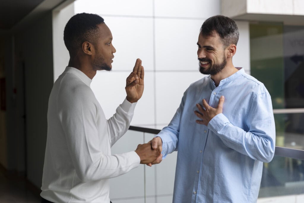 Um homem negro de roupa branca conversando com um homem branco de roupa azul