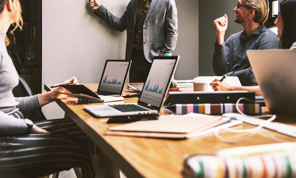 Reunião produtiva com profissionais participando ativamente de uma apresentação. Vários laptops na mesa mostrando gráficos e dados.